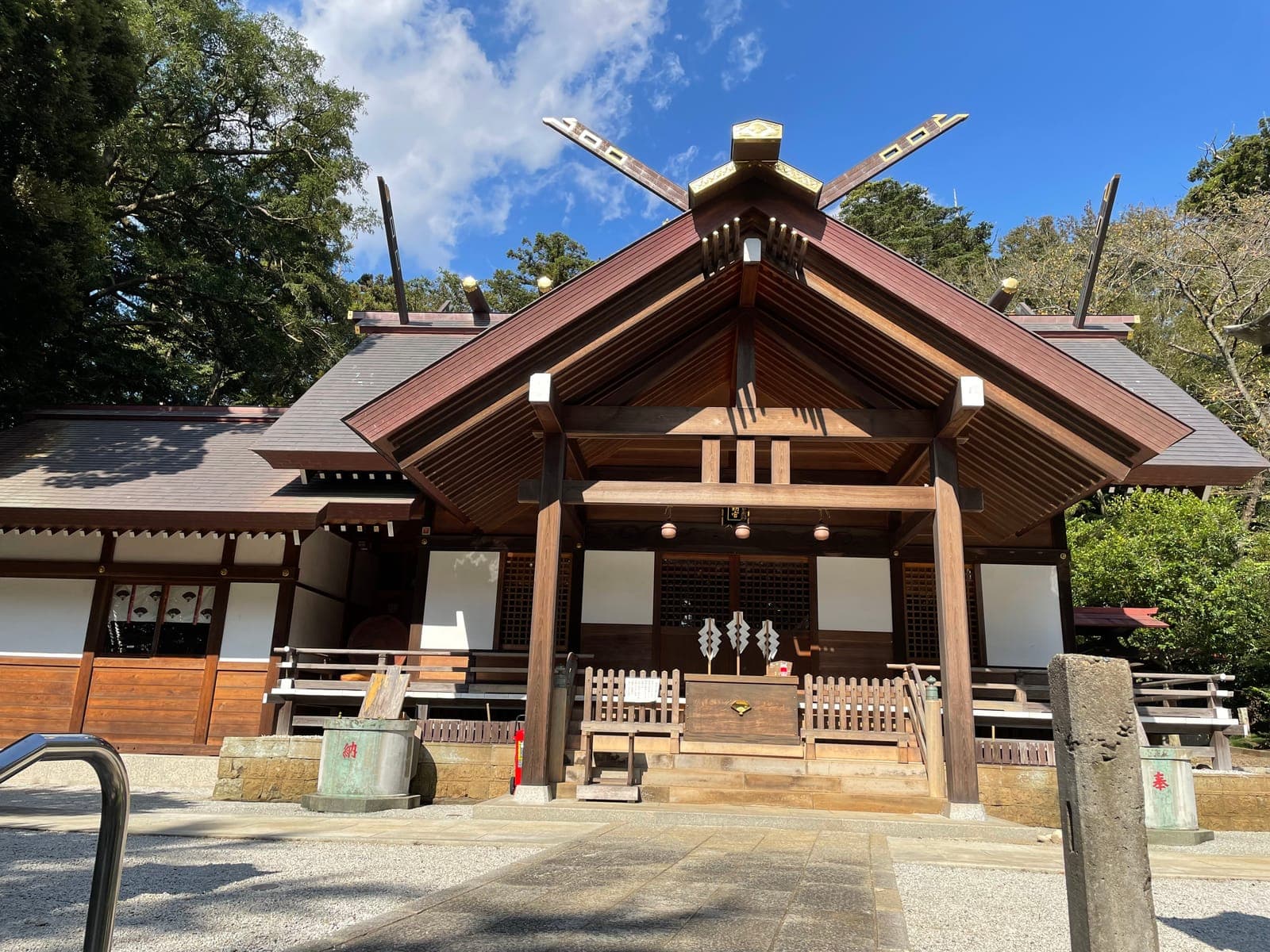 塚崎神明社の外観。木造の社殿で、急な切妻屋根があり、木々に囲まれて青空の下に建つ。