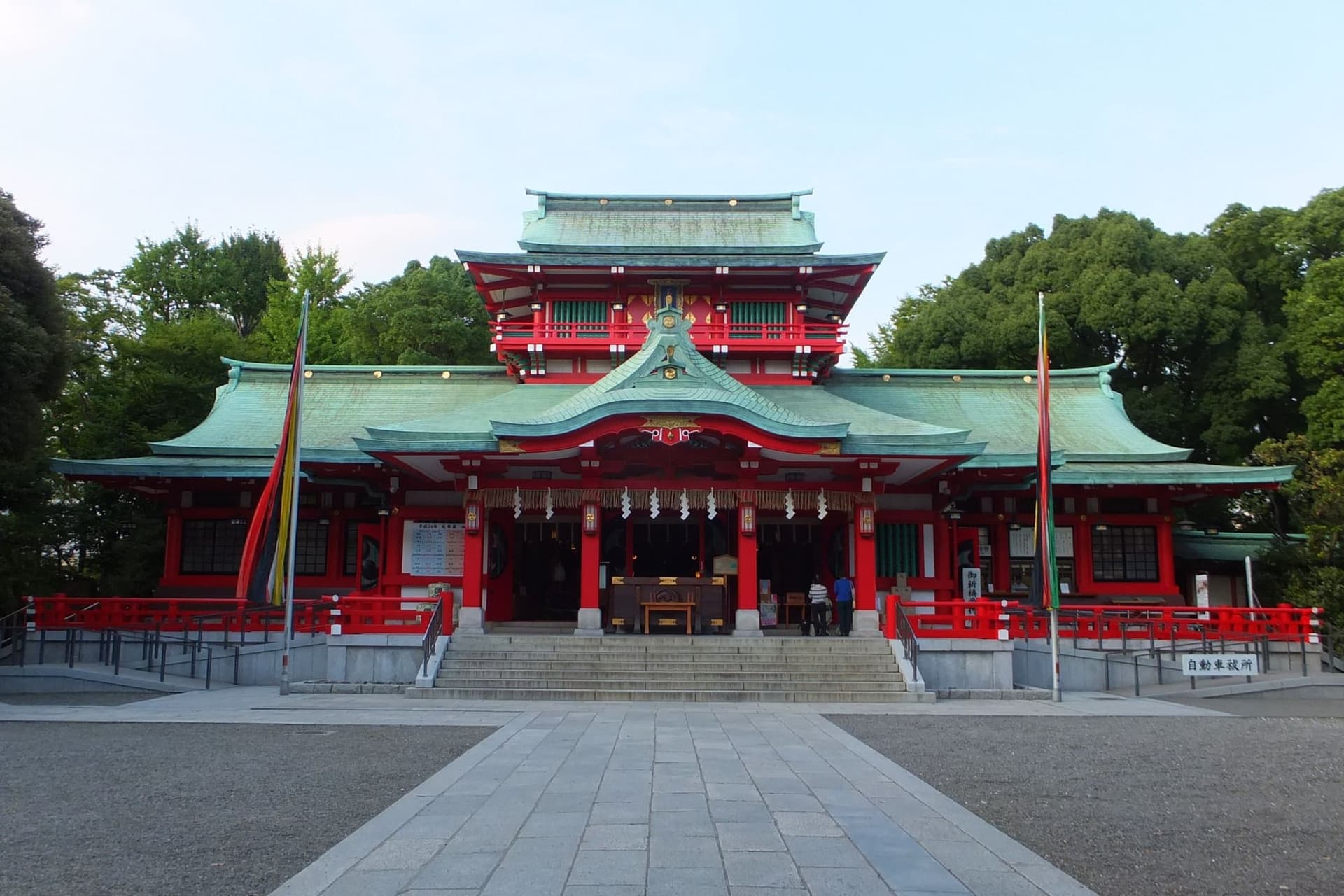 Edifício do santuário Tomioka Hachiman com paredes vermelhas, telhados verdes de cobre e um caminho de pedra até a entrada.