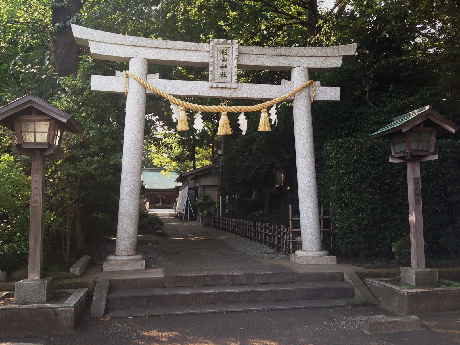 Torii en pierre de Hoshikawa Sugiyama, avec corde shimenawa et lanternes, ouvrant sur un chemin sous les arbres.