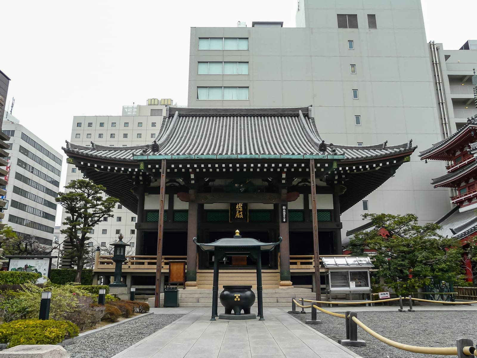 Exterior del templo Taiyu-ji, con techo de tejas, quemador de incienso central y edificios modernos al fondo.
