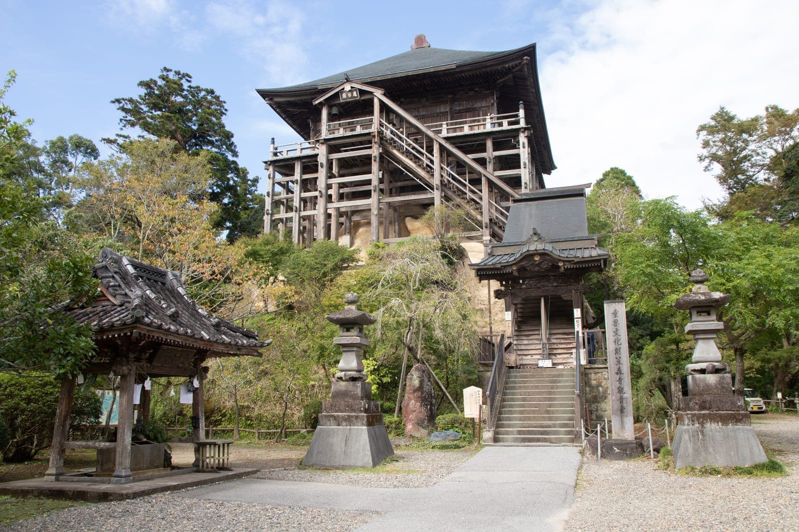 Kasamori-ji temple’s wooden main hall on a raised structure, with stairs, stone lanterns, and trees around it.