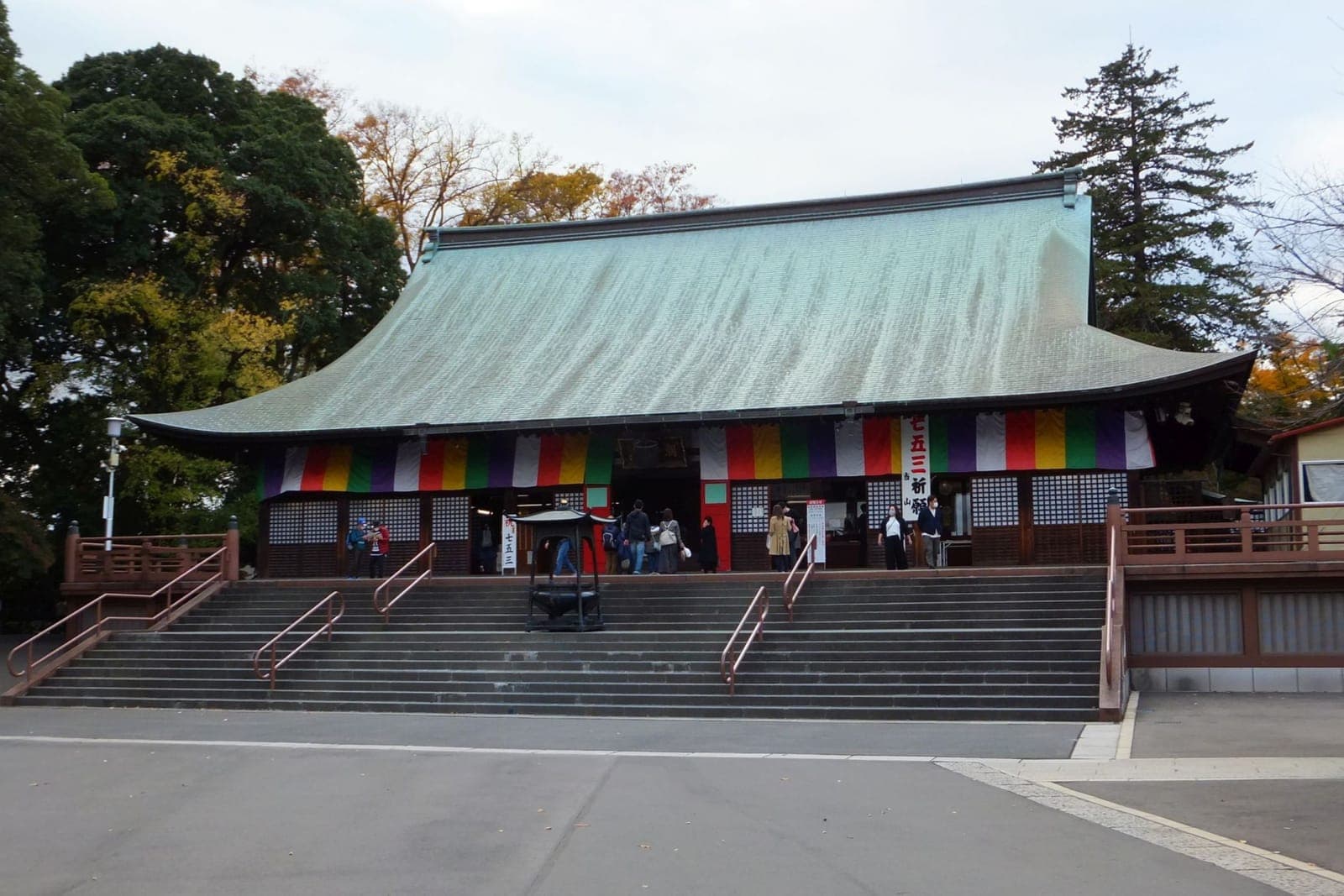 Salão do templo Kita-in com grande telhado curvo, faixas coloridas e visitantes na escadaria.