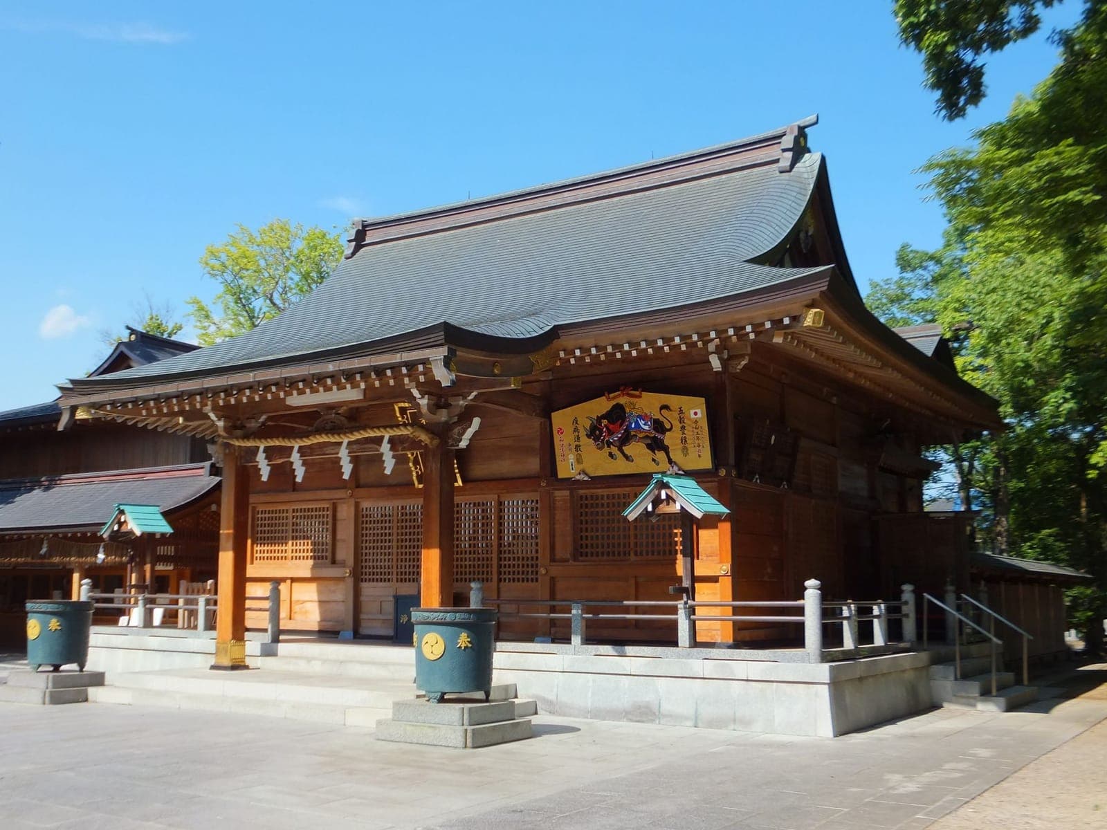 Exterior of Warabi shrine with a large wooden hall, curved roof, and trees under a clear blue sky.