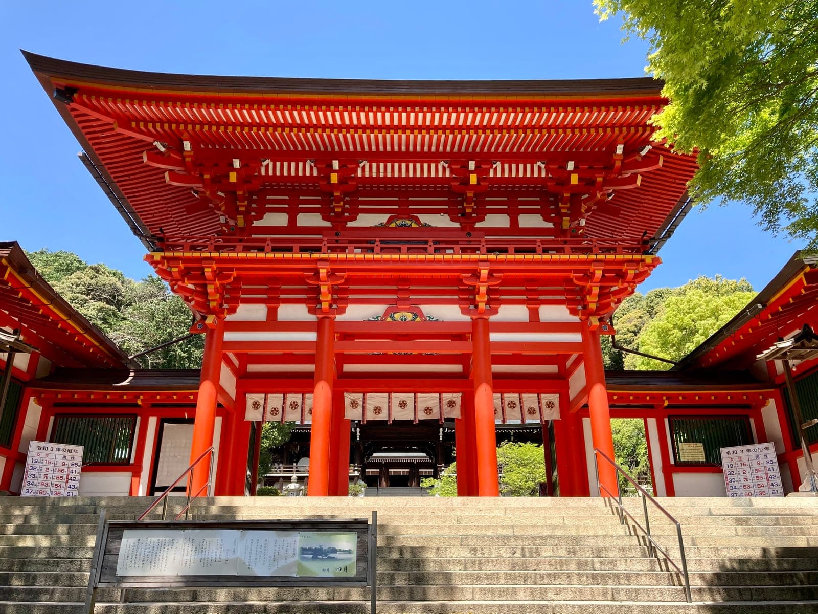 Portão romon vermelhão de dois andares de Omi Jingu no topo da escadaria de pedra sob um céu azul.