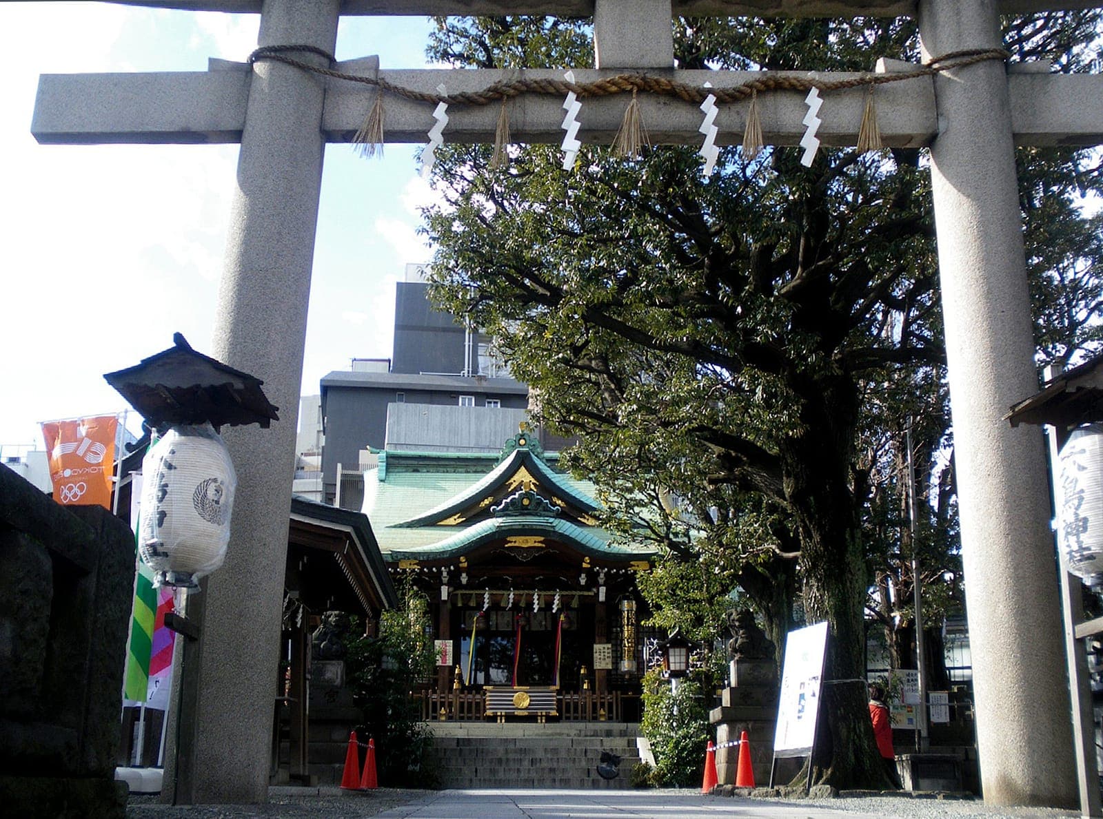 Un torii en pierre encadre l’entrée de Meguro Otori, avec le sanctuaire, des lanternes et un grand arbre.