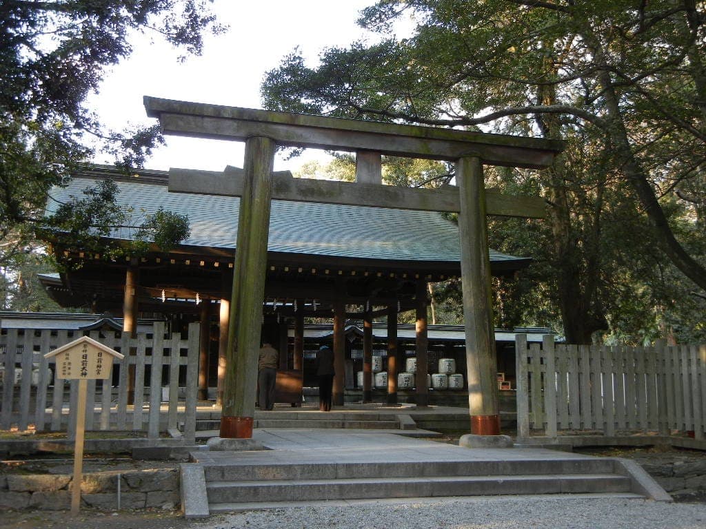 Torii gate at Nichizen-gu temple entrance, with a fenced shrine building and trees behind.