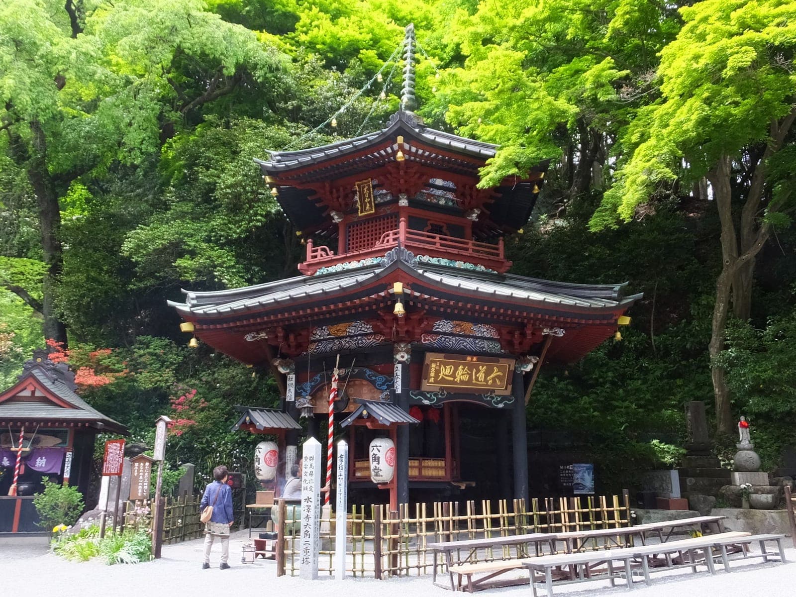 Edificio de Mizusawa-dera con techo de dos niveles, detalles de madera roja y faroles, rodeado de árboles verdes.