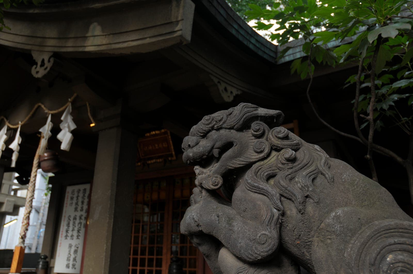 León guardián de piedra en la entrada de Inari Kio, con tiras de papel colgantes y hojas arriba.
