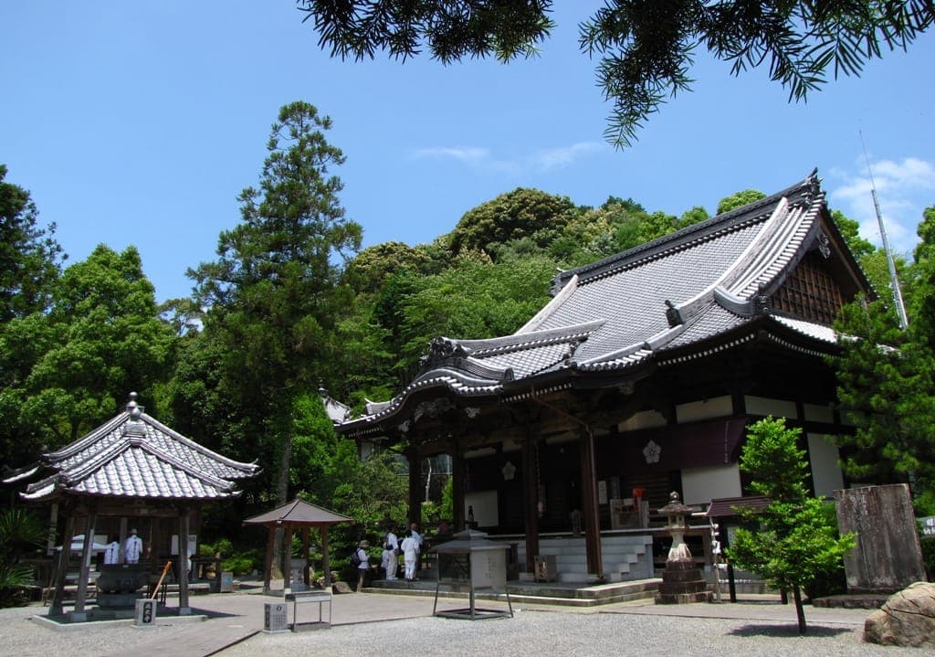 Edificios del templo Enko-ji con techos de tejas curvas, rodeados de árboles bajo un cielo azul.