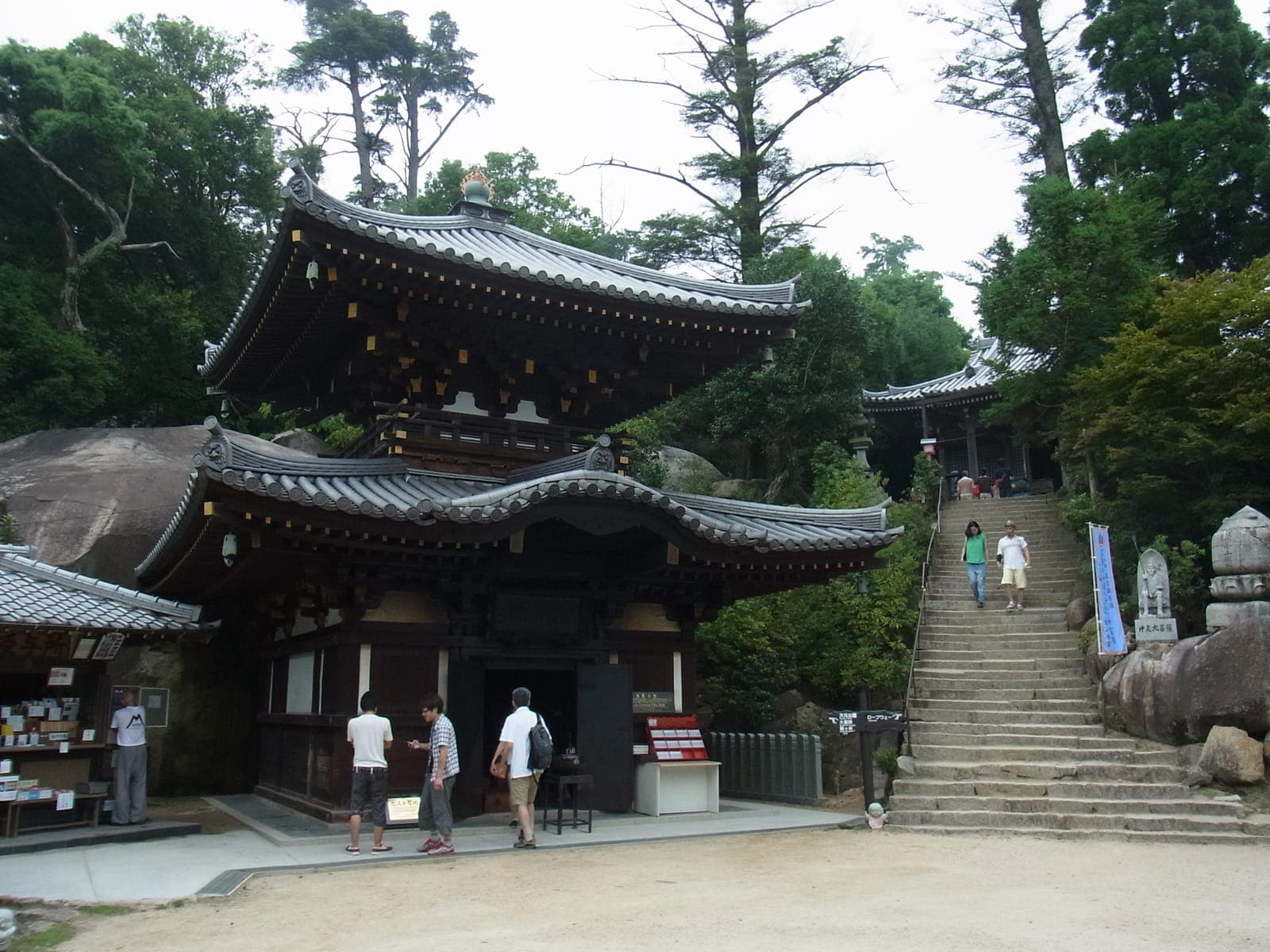 Edifícios do templo Reikado (Eternal Flame Hall) com telhados curvos de telhas, escadas de pedra, árvores e რამდენიმე visitantes.