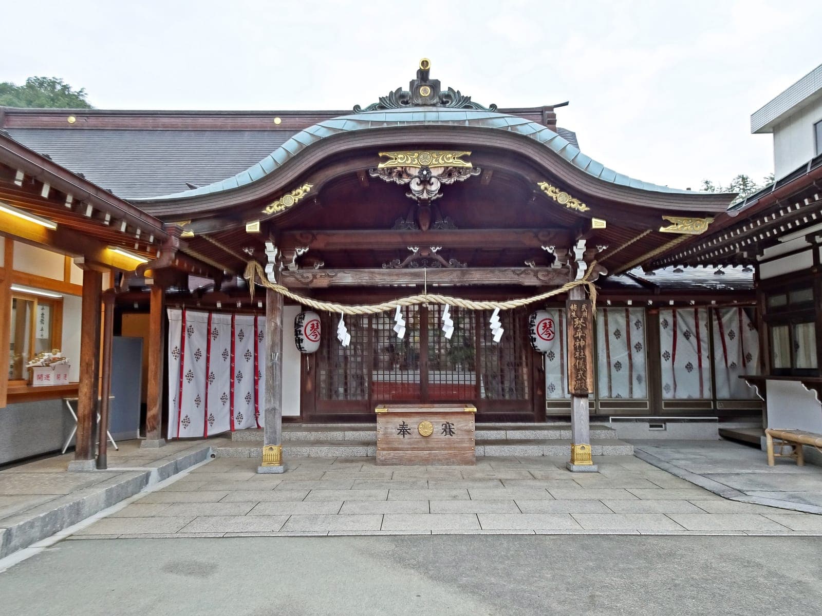 Exterior of Bushu Kakio Kotohira temple, showing a wooden shrine building with a curved roof, rope, lanterns, and stone-paved forecourt.