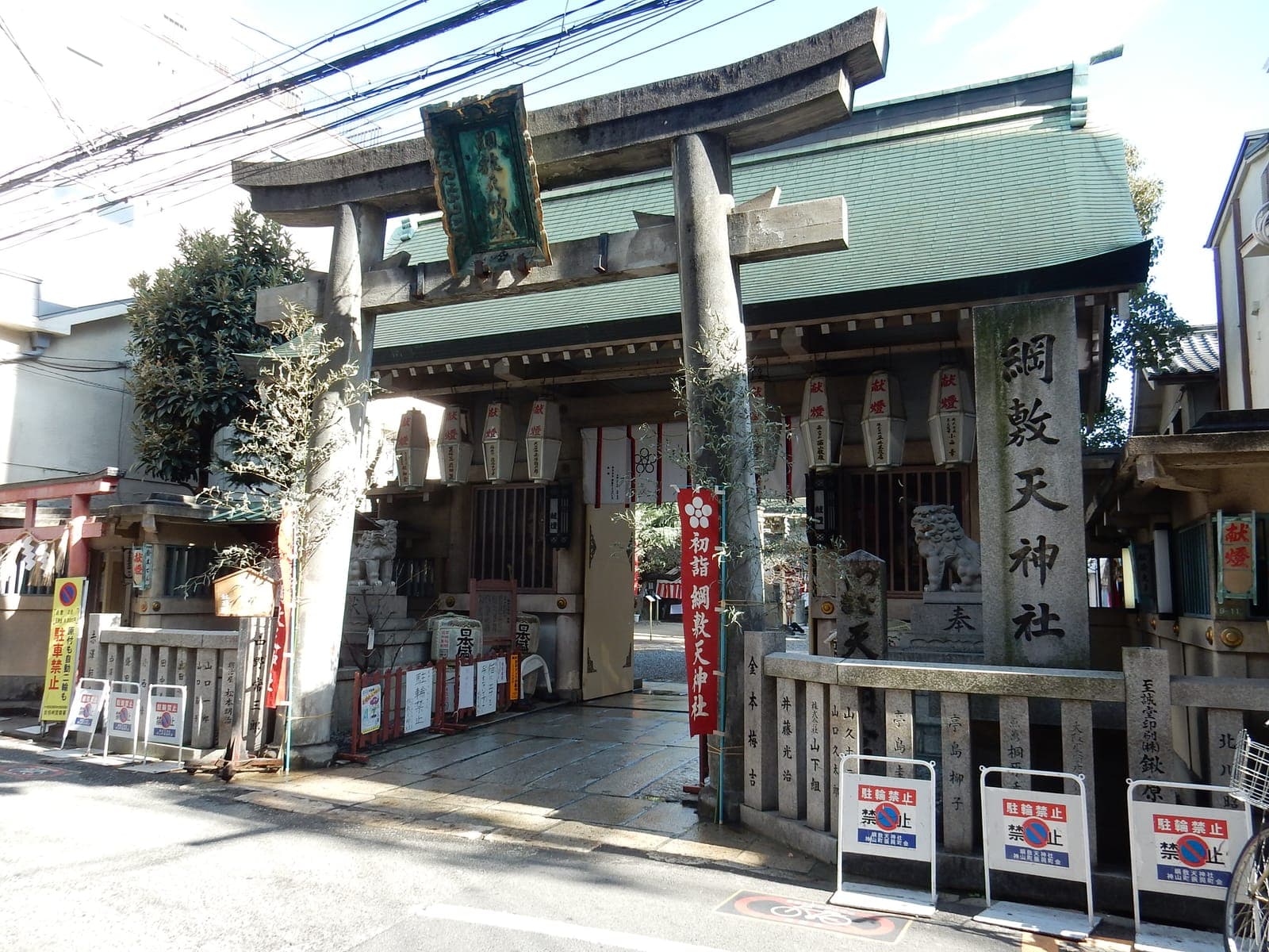 Exterior do Tsunashikiten Shrine Otabi Sha com torii de pedra, lanternas e telhado verde.