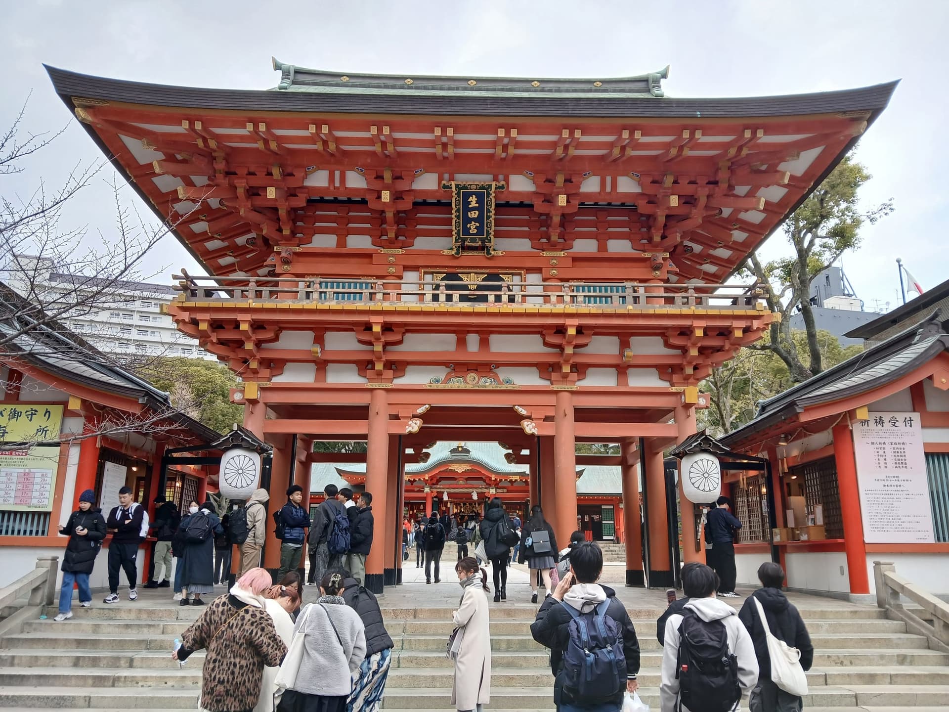 Portale rosso e bianco di Ikuta Jinja con lanterne e visitatori che passano sotto.