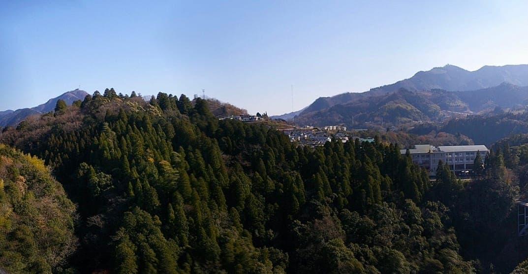 Montanhas cobertas de floresta sob céu azul, com Takachiho Jinja, Takachiho, Miyazaki ao fundo.