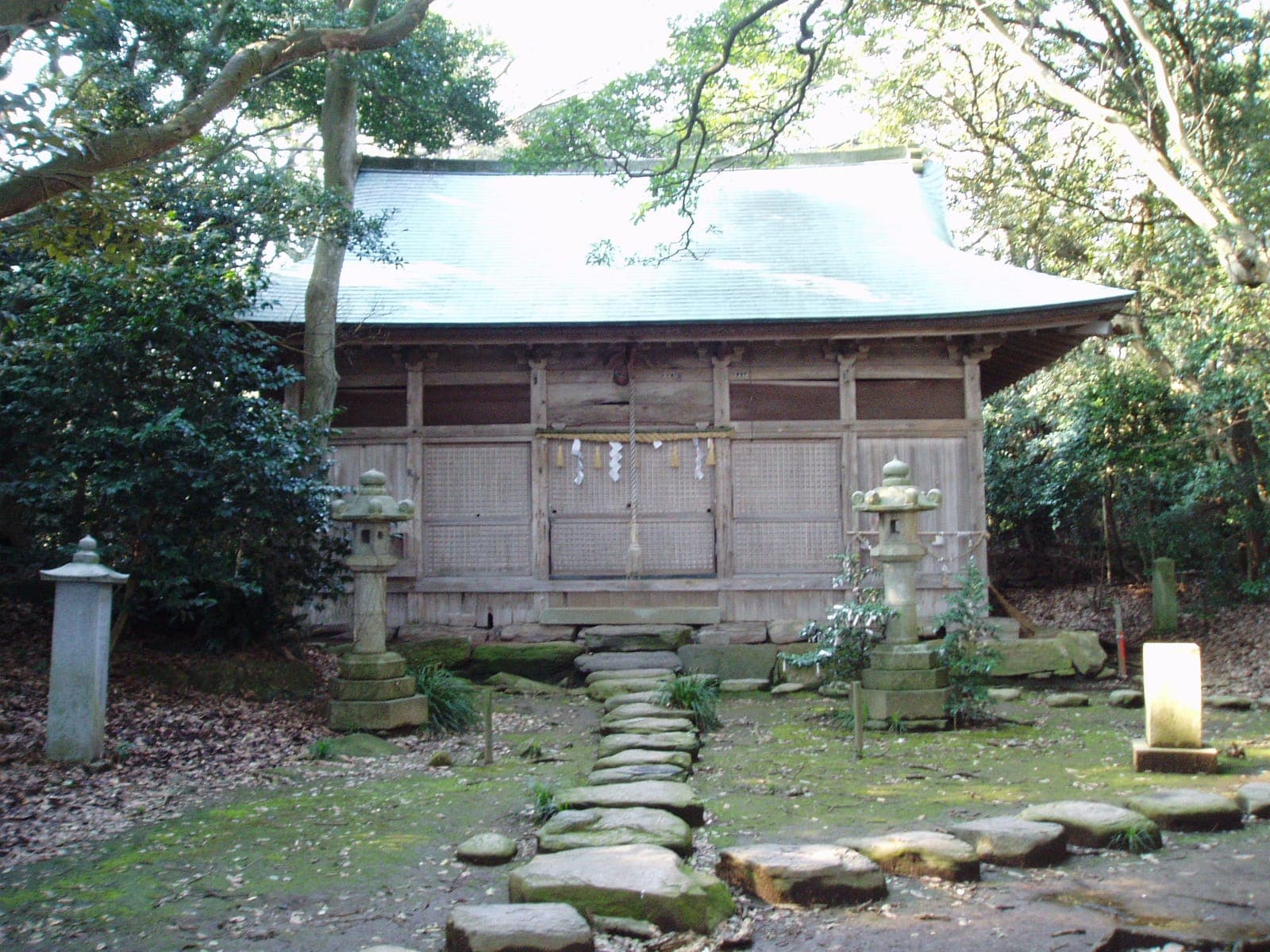 Exterior of Ominato shrine, a wooden building in a wooded area with stone lanterns and a stepping-stone path.
