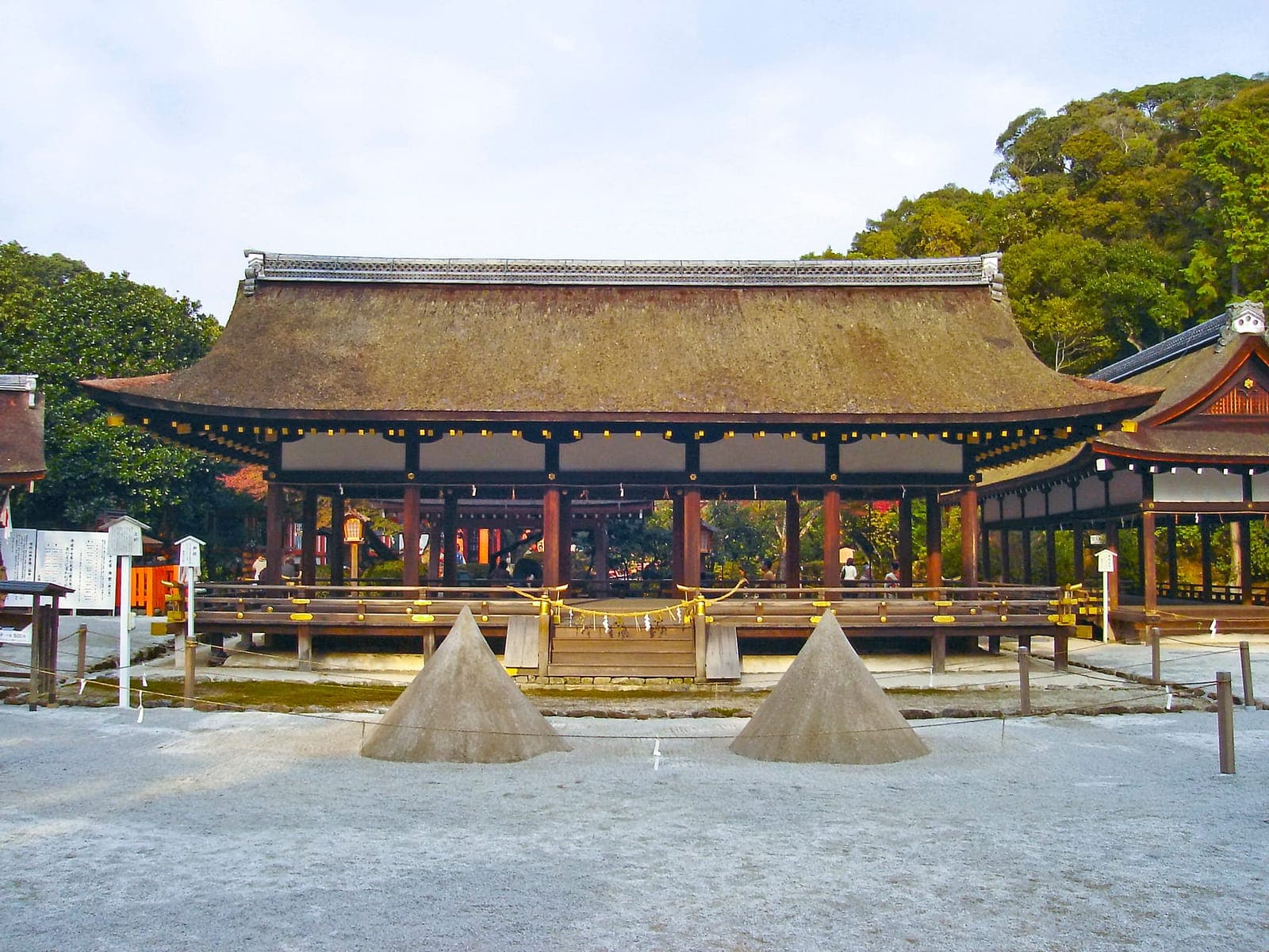 Extérieur du sanctuaire Agata Jinja, avec un grand hall au toit de chaume, une cour de gravier et des arbres.