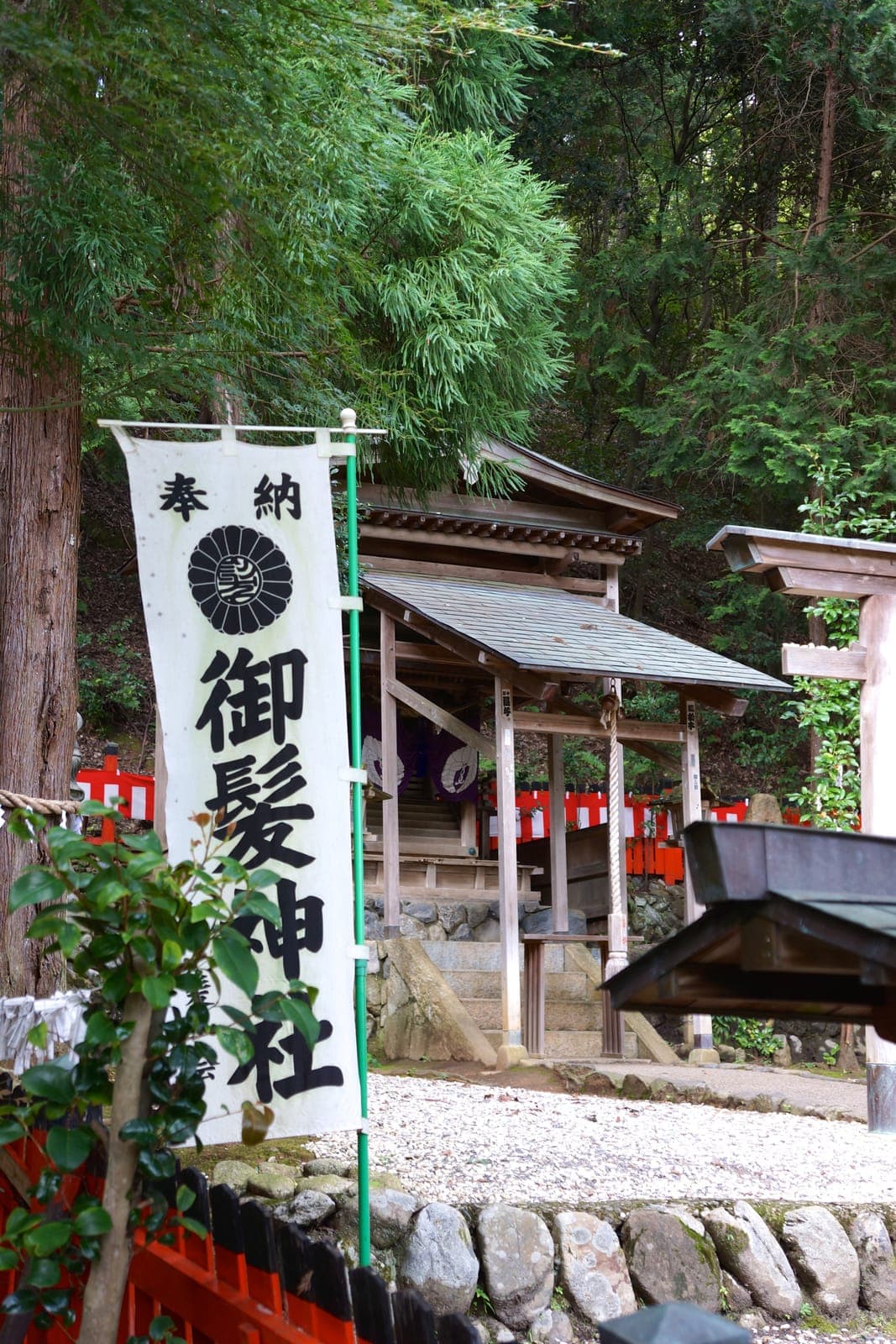 Small wooded shrine at Kyoto Saga Mikami Jinja with a white banner, stone steps, and red fence.