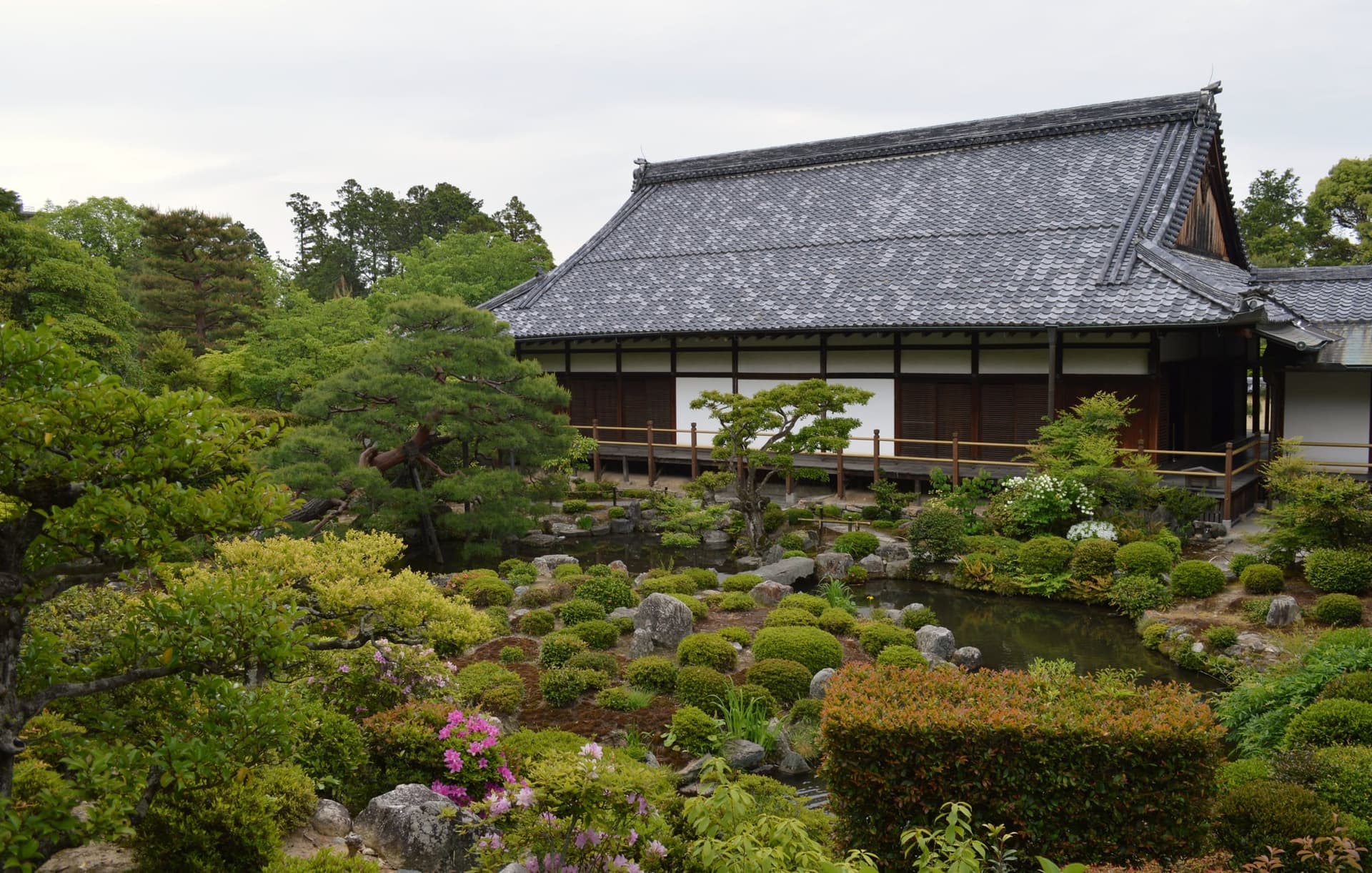 Exterior do templo Toji-in, com telhado de telhas, varanda de madeira e jardim com lago e arbustos.