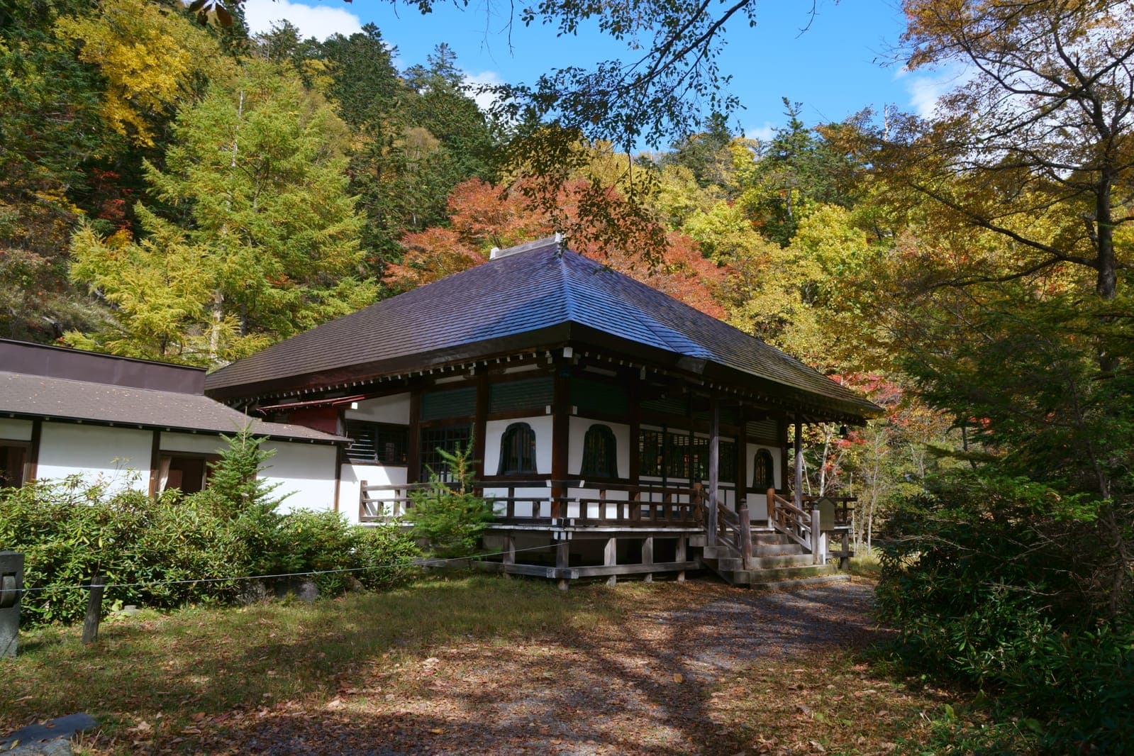 Nikkōzan Onsenji temple building with a dark roof, wooden porch, and autumn trees around it.