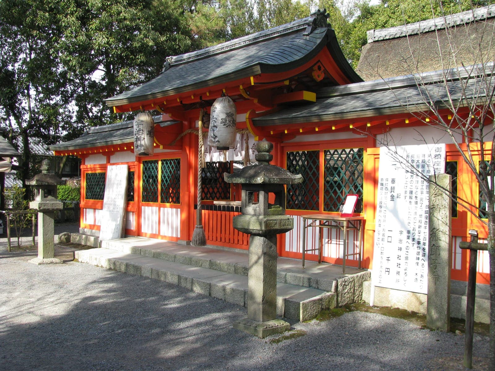 Esterno del santuario Uji con edificio rosso e bianco, lanterne appese, lanterne di pietra e alberi.