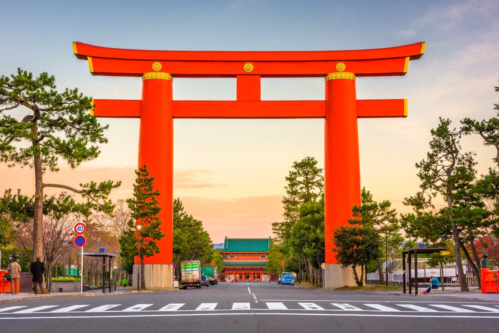 Gran torii roja de Heian Jingu sobre una carretera, con árboles y el santuario al fondo.