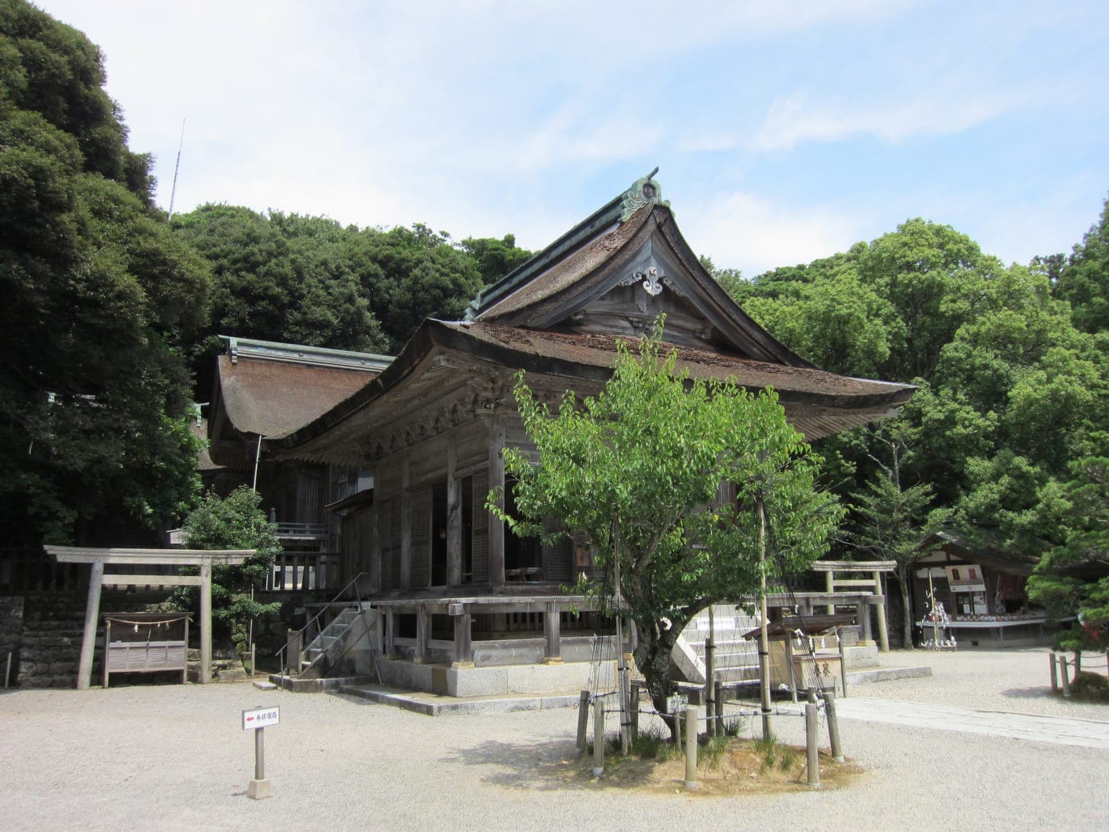 Gebäude des Keta Taisha mit geschwungenem Dach, umgeben von Bäumen und einem Kieshof.