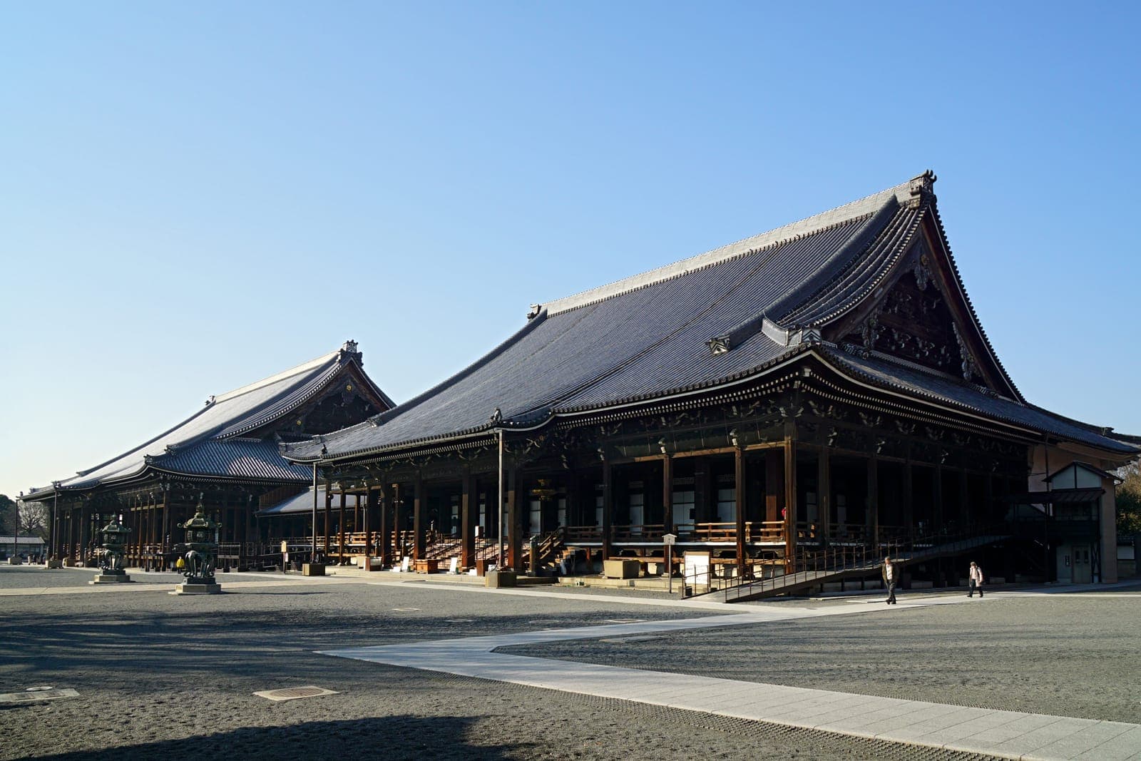 Extérieur de Nishi Hongan-ji avec deux grands halls en bois, de vastes toits en tuiles et une cour de gravier.