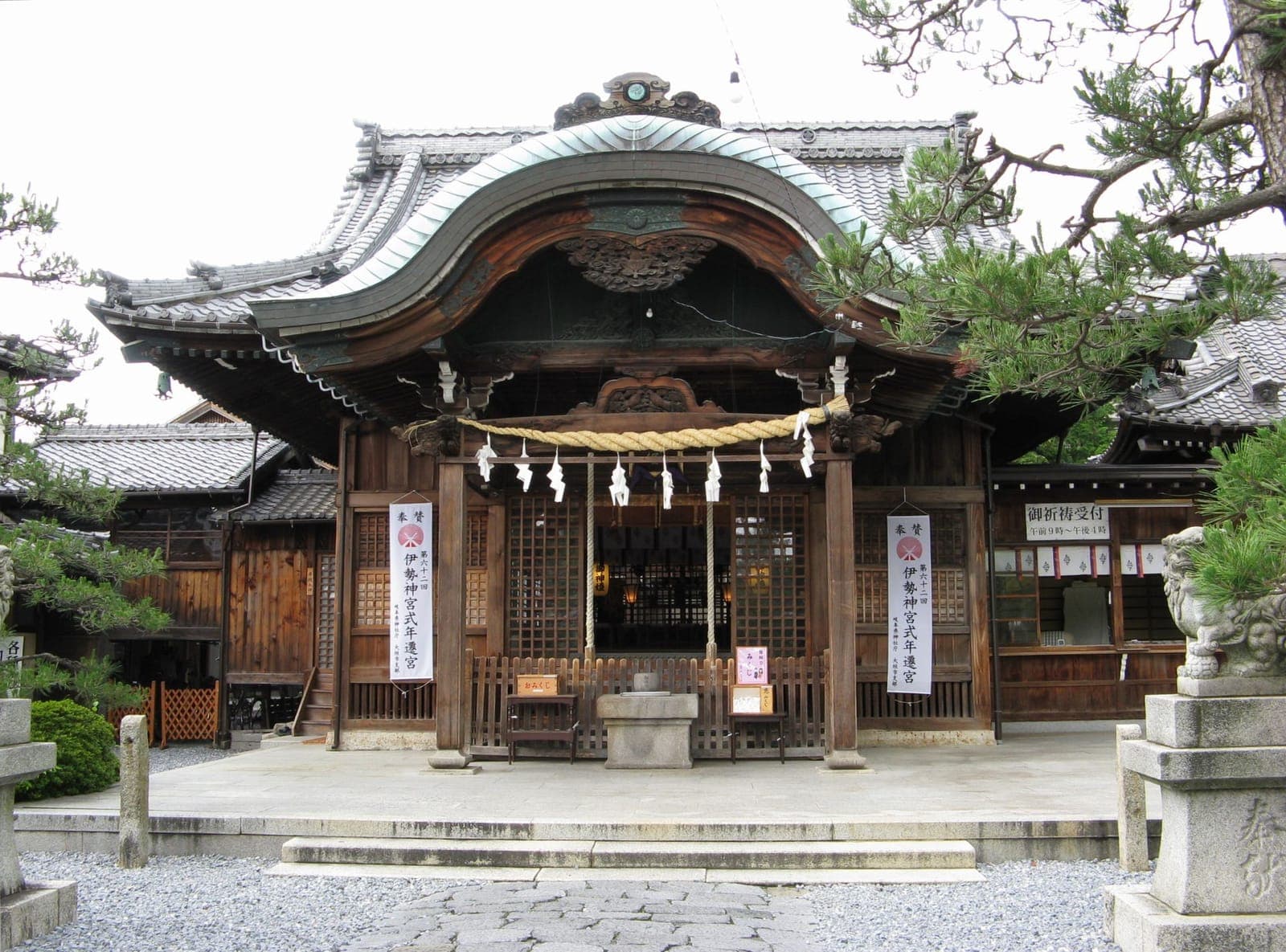 Exterior of Ogaki Hachim-An Jinja, a wooden shrine building with a curved tiled roof, rope ornament, and stone guardian statues.