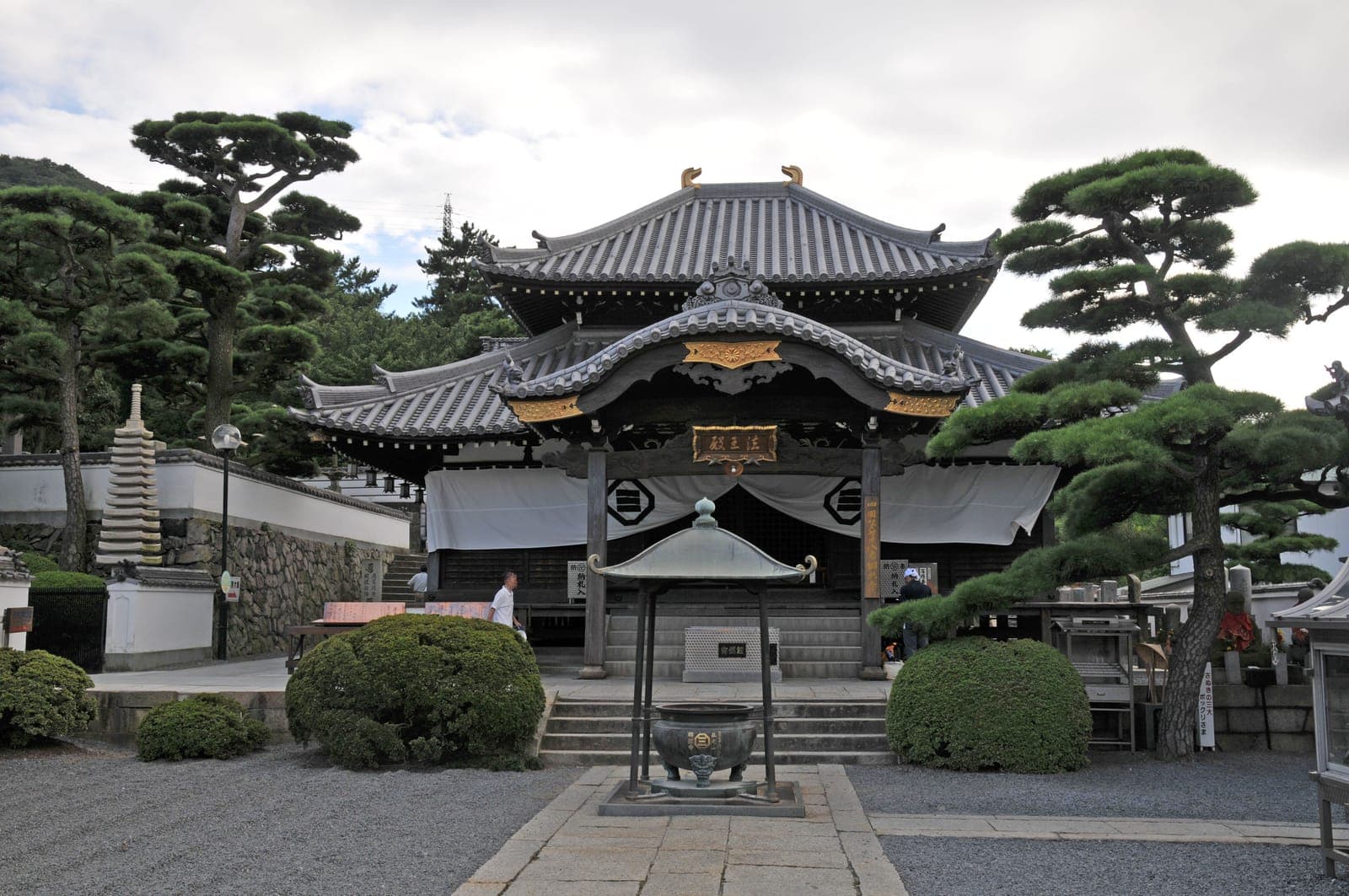 Esterno di 郷照寺 a Utazu, con sala dal tetto di tegole, pini potati, cortile di ghiaia e lanterna di pietra.