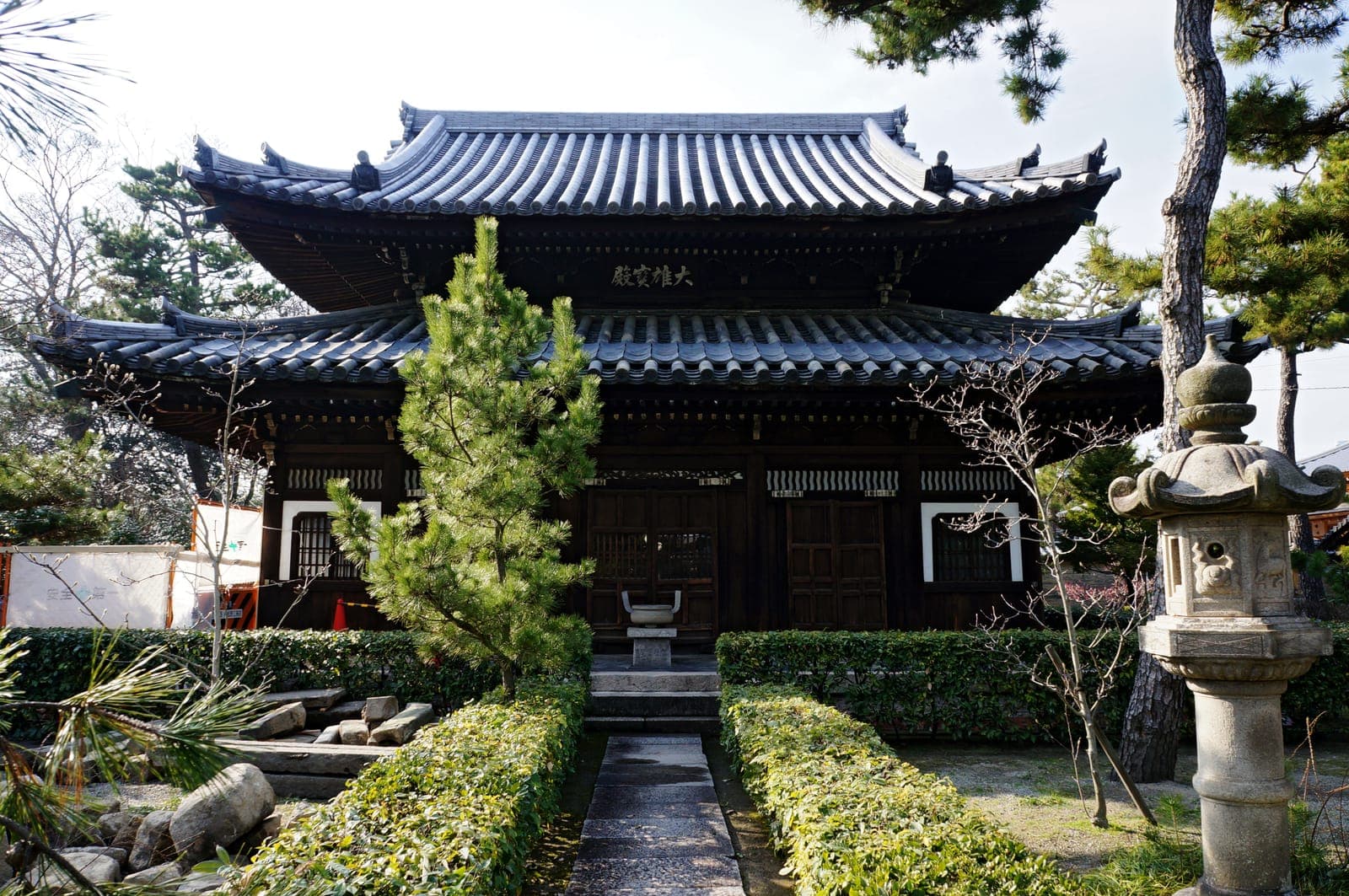 Nanshu-ji temple exterior with a dark tiled roof, wooden facade, garden path, pine trees, and a stone lantern.