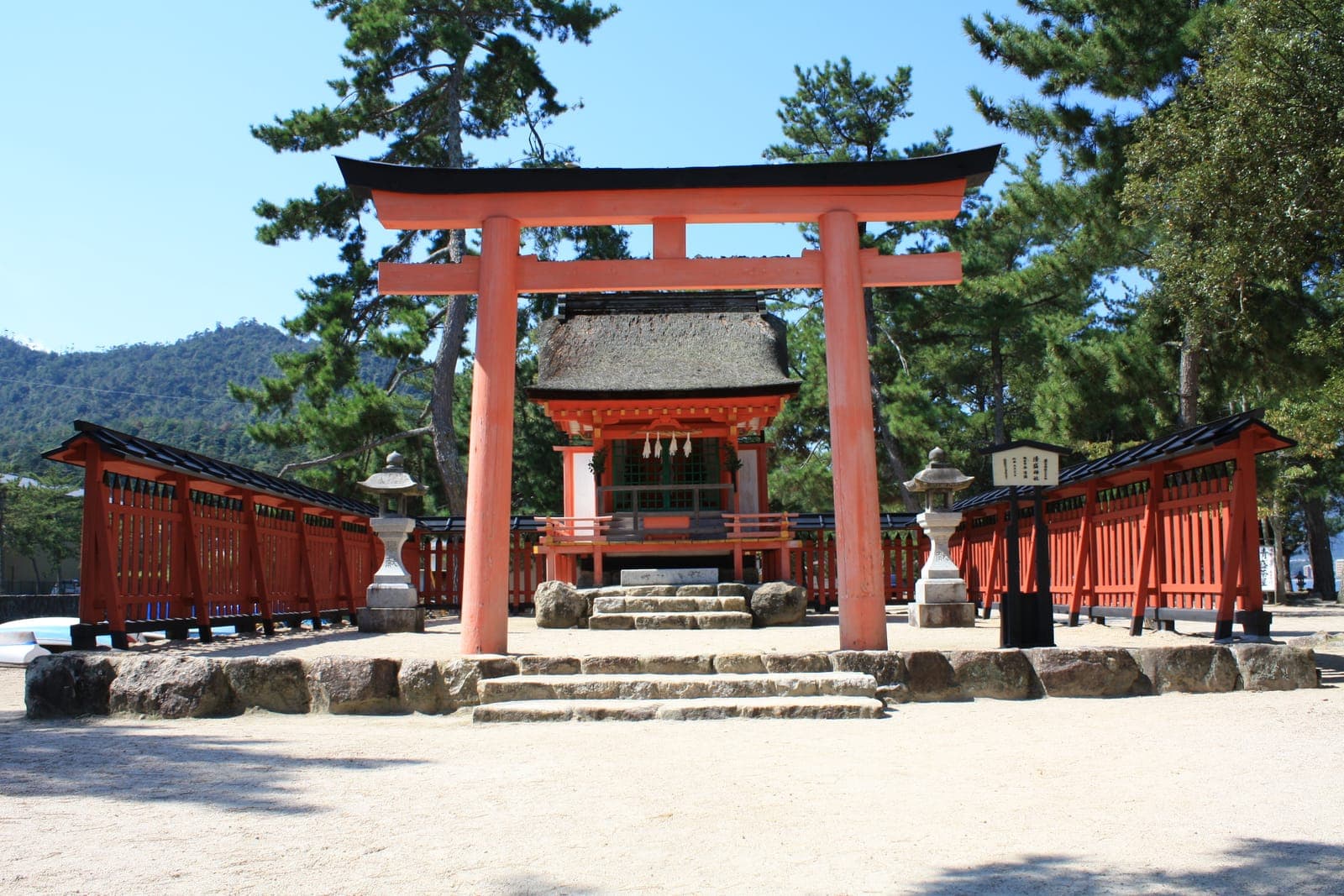 Exterior do Kiyomori Jinja com torii vermelho, santuário cercado, degraus de pedra e pinheiros.