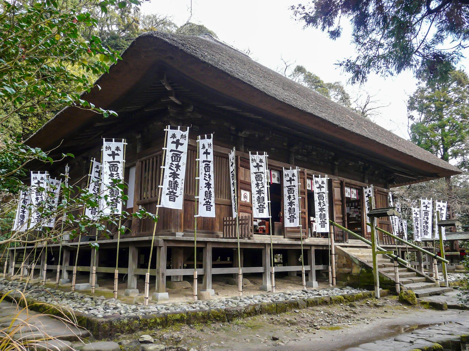 Holzgebäude des Tempels Sugimoto-dera mit Strohdach, Veranda und vielen weißen, senkrechten Bannern.