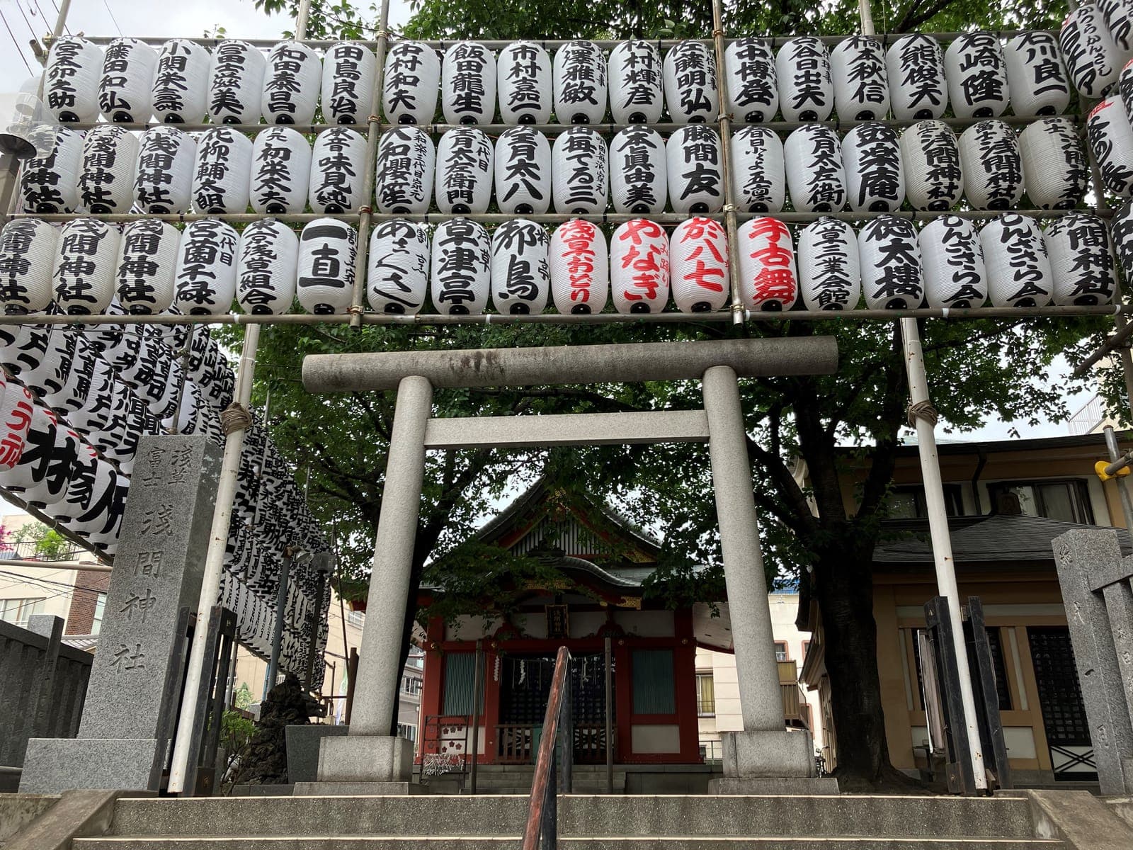 Torii en pierre devant Asakusa Fuji Sengen Jinja, avec des rangées de lanternes blanches au-dessus et un petit sanctuaire au fond.
